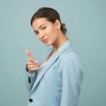 A young woman in a blue suit exhibits confidence with a relaxed pose against a blue background.