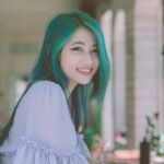 Beautiful young woman with vibrant green hair smiling happily indoors.